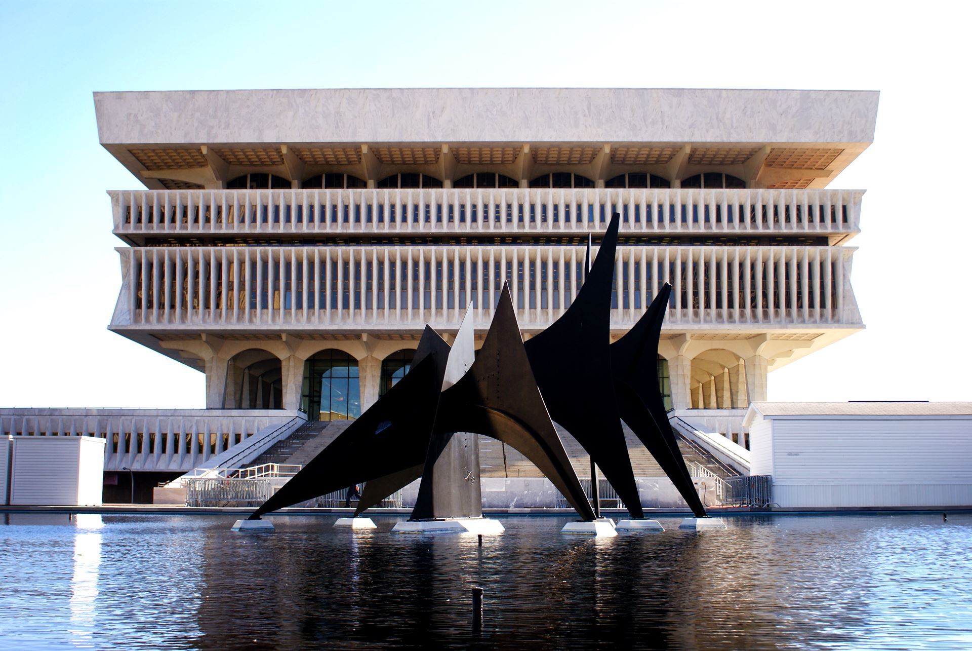 NYS Museum, a brutalist style architecture situated behind water with a large metal abstract sculpture